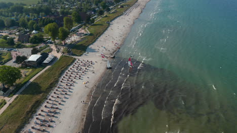 Aerial-drone-view-of-two-sailboats-in-tourist-beach-at-Baltic-sea-coastline,-Scharbeutz,-Germany,-circle-pan,-day